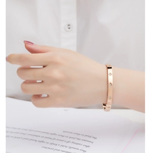 Close-up of a rose gold bangle with diamond-set four-leaf floral patterns on a wrist