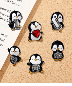 Macro detail of six enamel penguin brooches with rhinestones on cork background