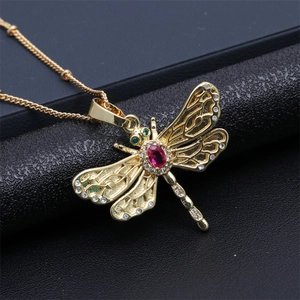 Detailed close-up of a golden dragonfly pendant with red and green zircons on a black base