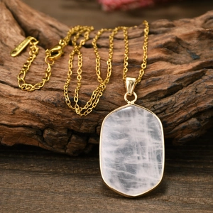 Macro shot of oval pink crystal pendant on gold chain over weathered wood texture