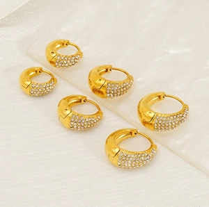 Détail des boucles d'oreilles huggie dorées avec pavage de cristaux blancs étincelants