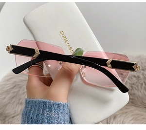 Detail of pink gradient rimless sunglasses with ornate golden metal temples on a white case