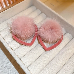 Close-up of pink heart-shaped earrings with fuzzy pom-poms on a velvet jewelry box