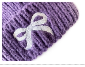 Close-up of purple chunky knit texture and embroidered bow detail on the winter hat
