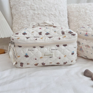 Detailed view of beige quilted makeup bag with bear and bread patterns on a bed