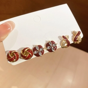 Detailed view of three pairs of wine red and gold festive earring sets on a display card