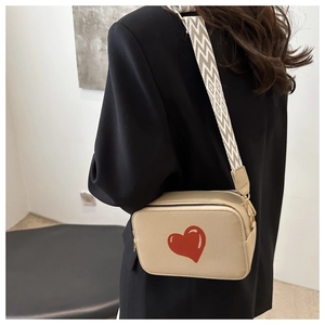 Detail of beige crossbody bag with red heart print and geometric pattern strap