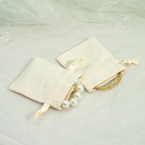 Macro shot of two beige cotton linen drawstring jewelry pouches with pearls and bracelet