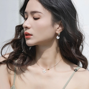 Close-up of model wearing daisy necklace and earring set with green gemstone accents