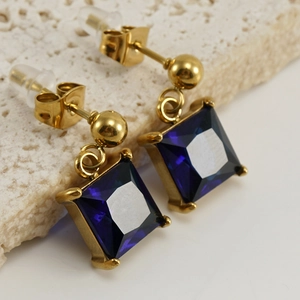 Macro shot of gold drop earrings with square-cut dark blue zircon on textured stone