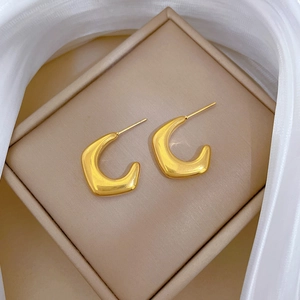 Detailed close-up of golden C-shaped titanium steel earrings on a beige jewelry box