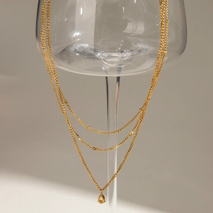 Detail of multi-layer gold necklace with teardrop pendant hanging on a glass