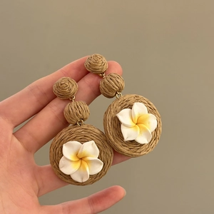 Dettaglio ravvicinato di orecchini in rafia fatti a mano con splendidi fiori di plumeria