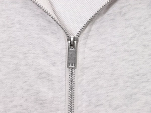 Detail of silver metal zipper closure on light grey heather knit sweatshirt fabric