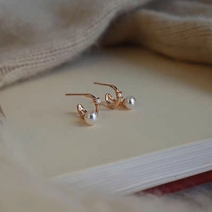Elegant rose gold C-shaped pearl stud earrings with sparkling zircon accents on book