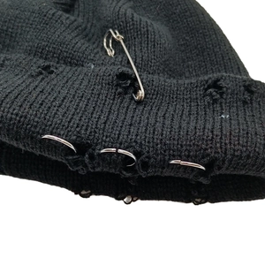 Détail d'un bonnet en maille noire avec épingles de sûreté et anneaux métalliques style punk