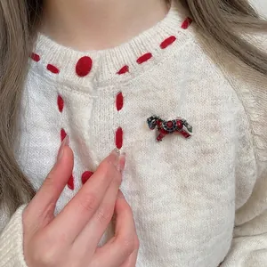 Broche cheval en émail rouge avec strass brillants sur un cardigan blanc à pois rouges