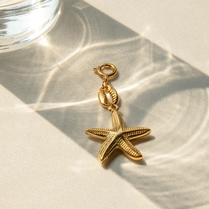 Golden starfish and shell metal pendant charms on beige fabric with elegant light shadows