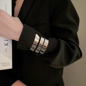 Dettaglio di bracciali geometrici in argento lucido indossati sopra una manica nera