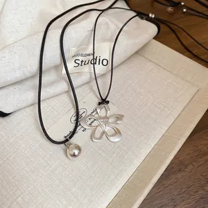 Silver hollow flower and ball pendant necklaces with black cord on wooden background
