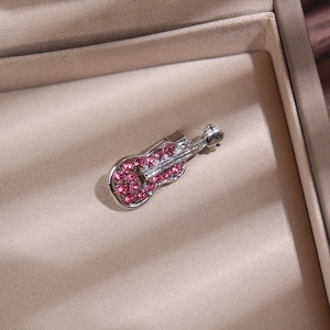 Détail d'une broche guitare argentée avec strass roses dans un écrin à bijoux beige