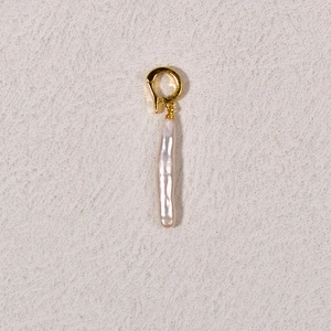 Detail shot of a refined baroque pearl pendant with a golden metal clasp on a textured surface