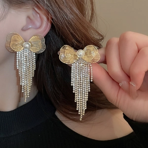 Close-up of golden bow-shaped tassel earrings with pearl and shimmering rhinestones