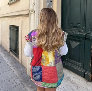 Street view of a woman wearing a colorful patchwork quilted vest with ethnic floral patterns
