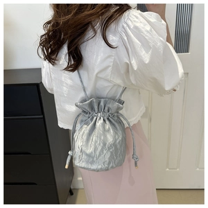 Detail of silver drawstring bucket bag with pleated metallic texture worn by a model
