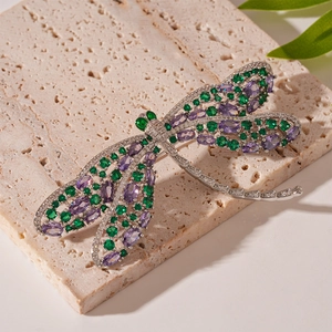 Macro detail of a dragonfly brooch with green and purple zircons on a beige travertine stone