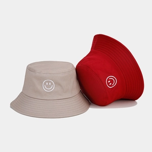 Détail de bobs en coton kaki et rouge avec broderie minimaliste de logo visage souriant
