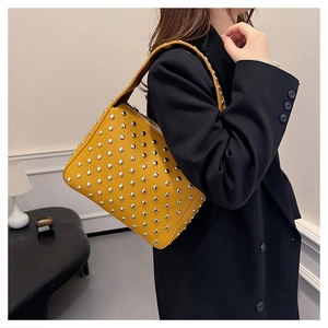 Detail of yellow lychee leather shoulder bag with silver rivet studs on a female model