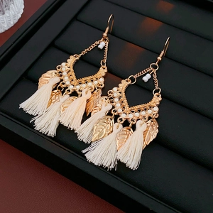 Detailed macro view of bohemian gold leaf earrings with beige tassels and white beads