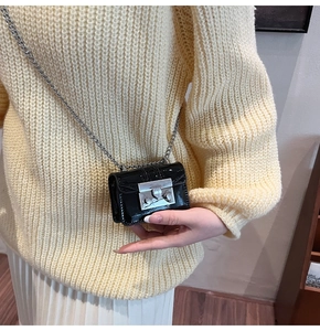 Close-up of a mini black patent leather crossbody bag with silver chain on yellow sweater