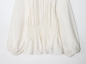 Detail of white pleated blouse featuring elastic waist and elegant lantern sleeves