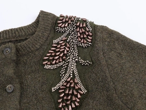 Dettaglio del cardigan in maglia verde oliva con ricami di perline in bronzo sulla spalla