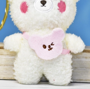 Macro detail of a small white fuzzy bear plush toy keychain wearing a cute pink bear bag.