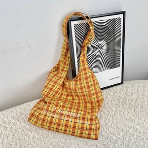 Detail of yellow checkered canvas tote bag with embroidered text and soft fabric texture