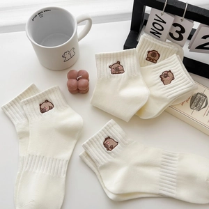 Dettaglio di calze color crema con ricamo capybara su una scrivania in stile lifestyle