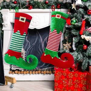 Festive red and green elf-style Christmas stockings with bells on a fireplace mantle