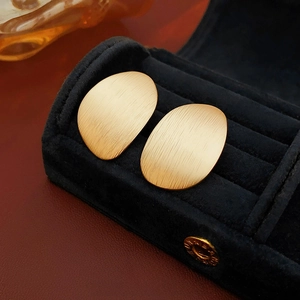 Macro detail of golden matte brushed irregular oval stud earrings in a premium jewelry box