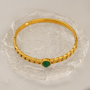 Detailed view of a gold Cuban link bangle featuring a centered green round gemstone