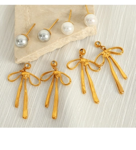 Detailed macro shot of golden bow drop earrings and elegant pearl studs on stone