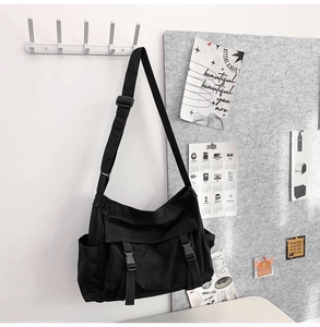Détail d'un sac messager en toile noire avec boucles frontales et poches latérales sur un mur