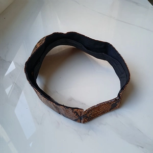 Brown faux leather snakeskin print headband with black fabric lining on marble background