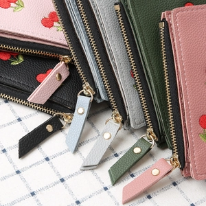 Close-up of litchi grain leather wallets featuring cherry embroidery and gold zippers