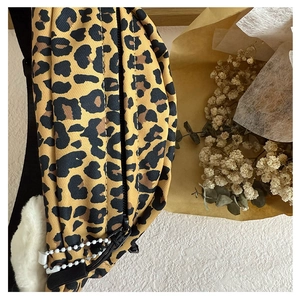 Detail view of leopard print canvas waist bag featuring a white plush ball and bead chain