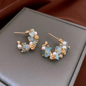 Detailed shot of C-shaped gold earrings with aquamarine stones and white pearls on velvet