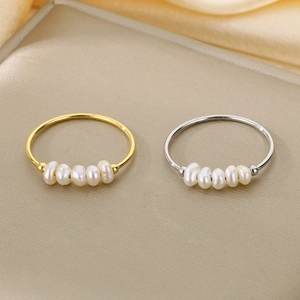 Vista macro di anelli in titanio oro e argento con cinque delicate perle d'acqua dolce