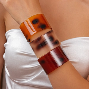 Detail of stacked wide tortoise shell acetate bracelets in brown and amber resin